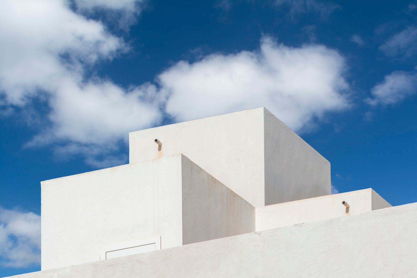 Abstract view of a modern minimalist white building under a vibrant blue sky with clouds.