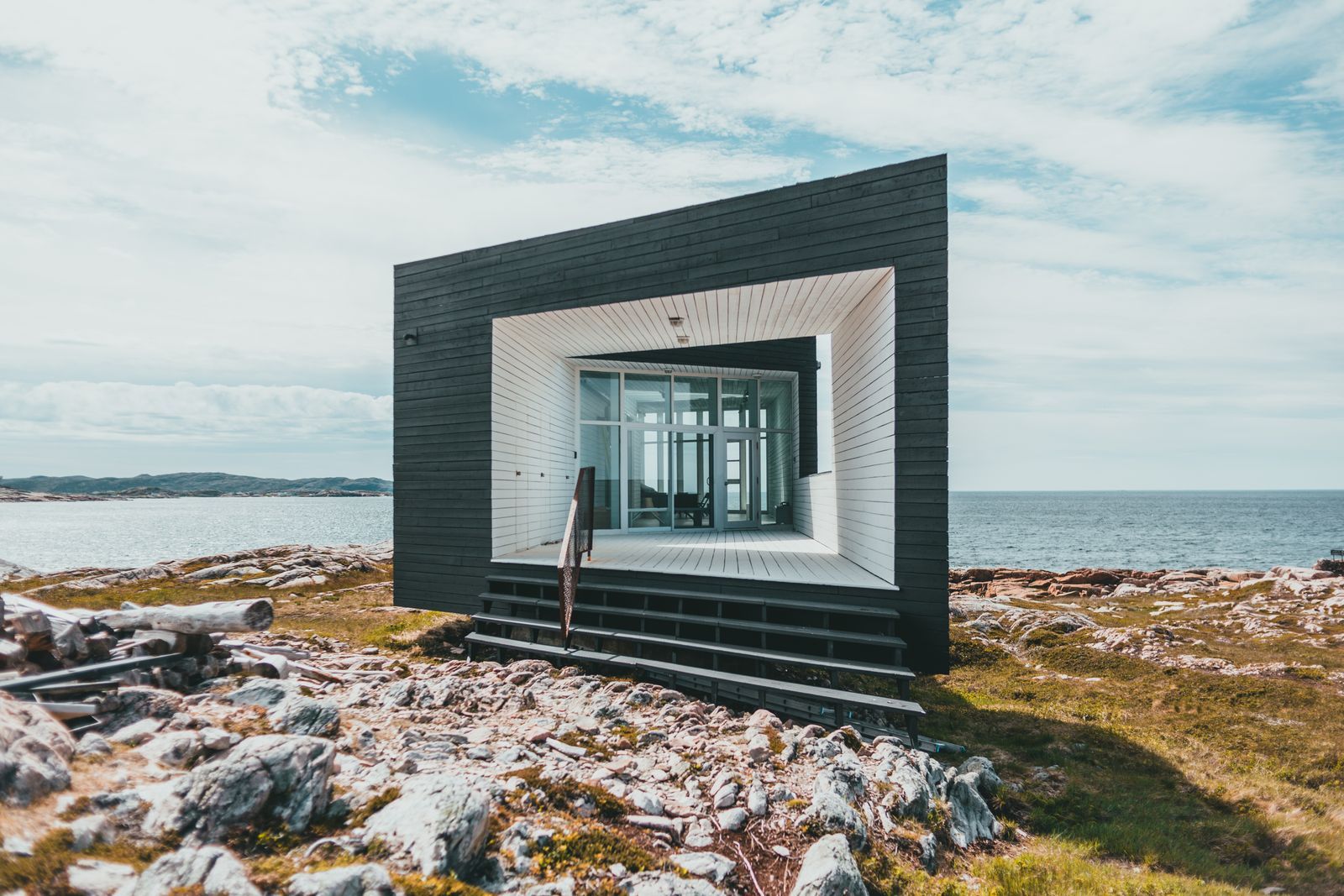 Contemporary tiny house on rocky coast with ocean view, showcasing minimalist architecture.